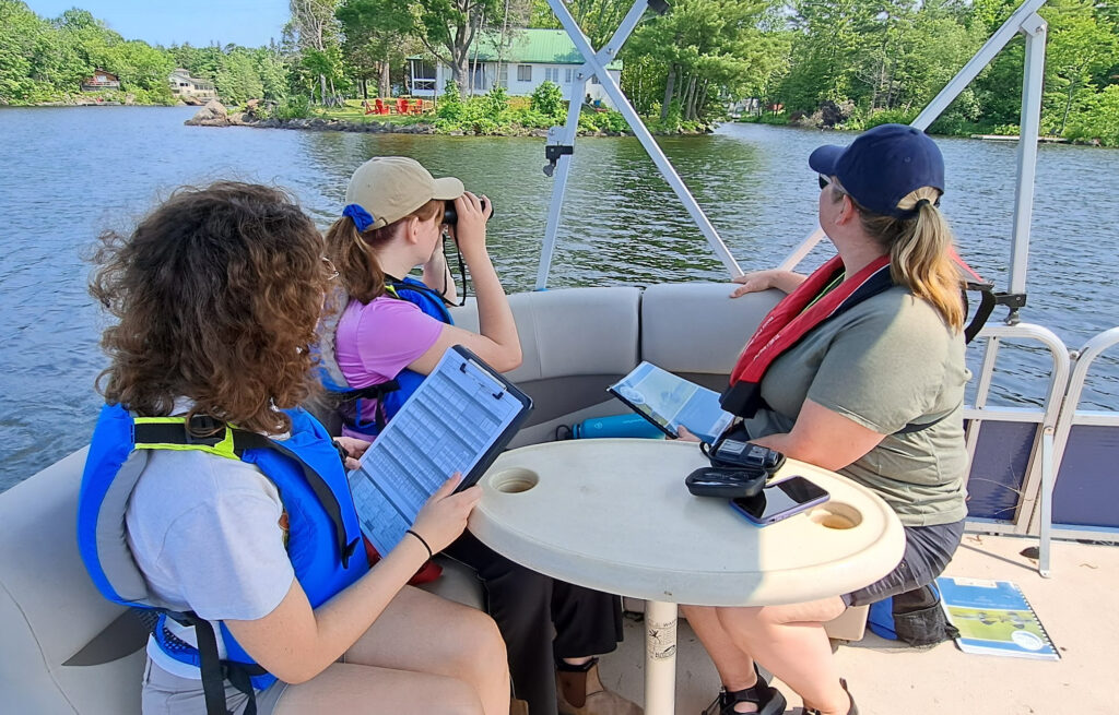 Photo of three female assessors in a boat looking at a lake shoreline as part of the Love Your lake program